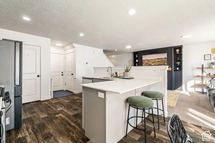 Kitchen featuring an island with a peninsula-style breakfast bar, quartz countertops, recessed lighting, and wood-finish flooring, complemented by built-in dark-toned shelving