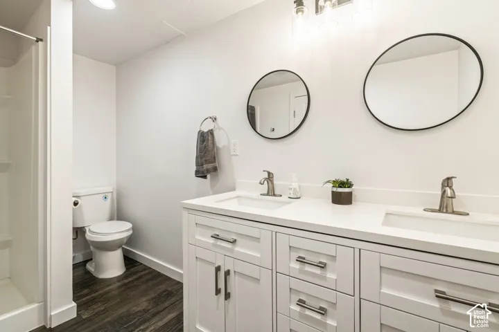 Double vanity featuring white cabinetry, a solid surface countertop with integrated dual sinks, brushed metal faucets, round wall-mounted mirrors, and wood-finish flooring