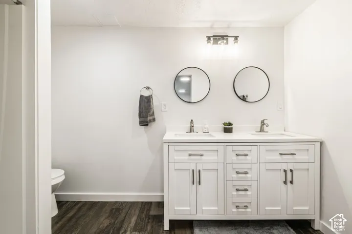 White dual-sink vanity with a solid surface countertop, metallic hardware, dual round mirrors, and a three-light fixture over wood-finish flooring