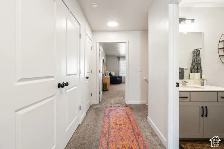 Hallway featuring recessed ceiling lighting, multiple solid-panel doors with matte black hardware, and a bathroom vanity with a neutral-tone finish and stone-surface countertop