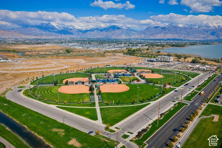 Aerial perspective featuring a multi-field baseball complex with paved parking, expansive green space, and mountain backdrops