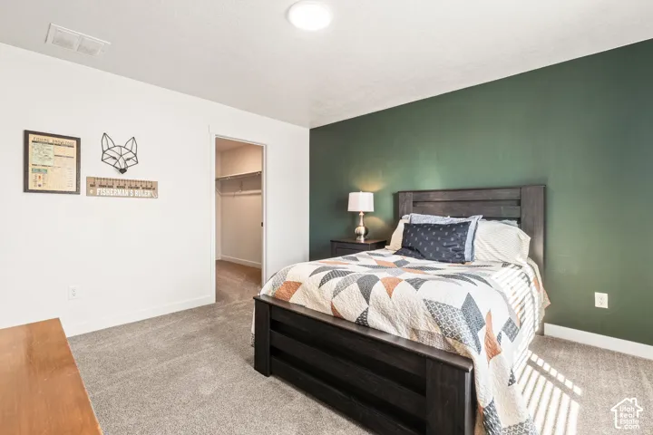 Bedroom featuring a forest green accent wall, neutral carpeting, and a walk-in closet with built-in shelving