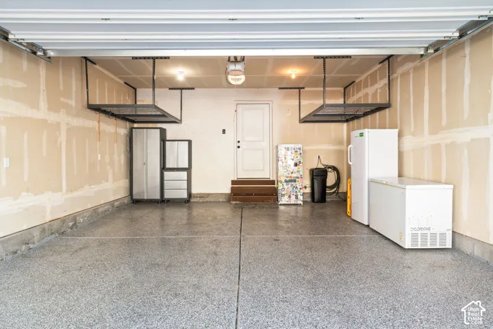 Two-car garage featuring epoxy-coated flooring, elevated metal ceiling storage racks, and an exterior access door