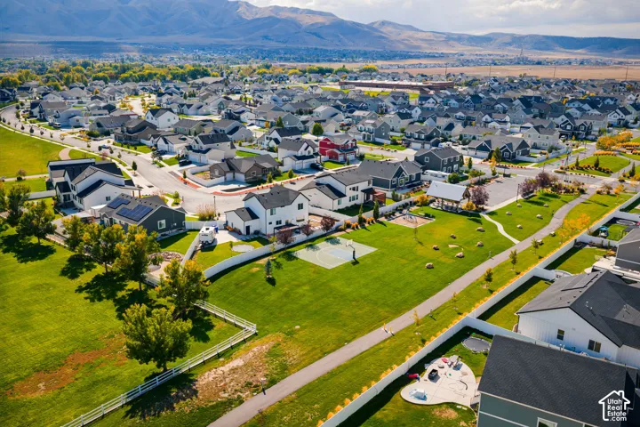 Aerial perspective of a suburban neighborhood featuring paved walking paths, a multi-use sports court, expansive green space, and mountain backdrops