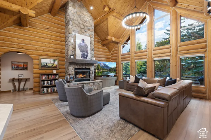 Living area featuring high vaulted ceiling, a fireplace, light wood-type flooring, log walls, and a wooden ceiling with exposed beams