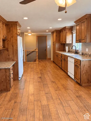 Kitchen featuring wood-finish flooring, custom wood cabinetry, stone-finish countertops, recessed lighting, and a dual-basin sink with a high-arch faucet