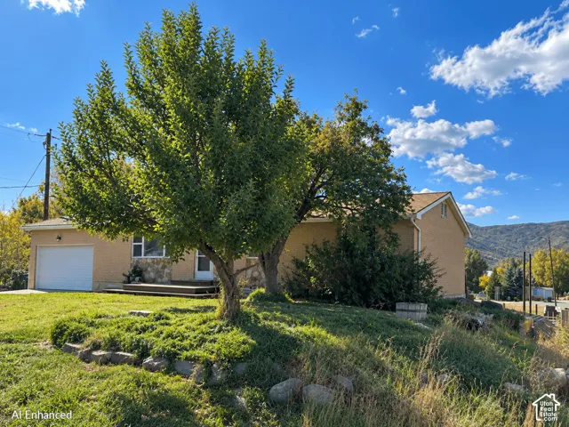 Brick exterior with stone facade accents, attached single-car garage, and tiered landscaping with mature trees and mountain backdrop