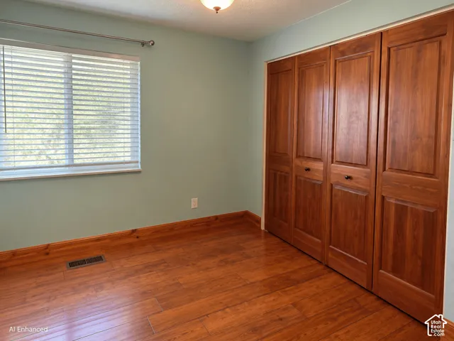 Wood-finish flooring, natural wood-tone paneled closet doors, and a window with horizontal blinds