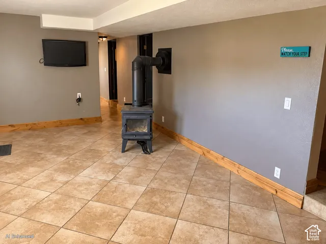 Freestanding cast iron stove with matte black finish, neutral tile flooring laid on a diagonal, and natural wood trim accents