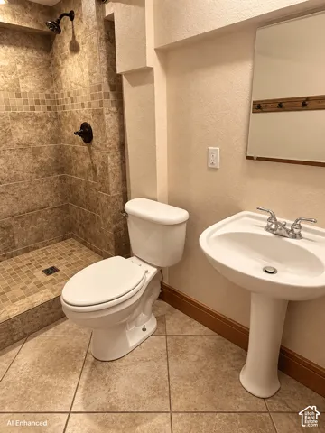 Walk-in shower featuring natural stone-finish wall tile, mosaic floor tiling, and dark bronze-tone fixtures, complemented by a white pedestal sink and neutral stone-finish floor tile