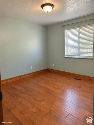 Room interior featuring wood-finish flooring, natural-tone wall paint, a window equipped with horizontal blinds, and a semi-flush mount ceiling fixture