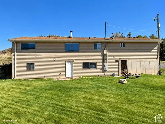 Two-story exterior featuring tan horizontal siding, a shallow-pitched roof with a central chimney, dual-pane windows, and a concrete foundation base with integrated storage