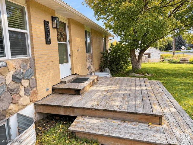 Exterior facade featuring light-toned brickwork, natural stone accents, a wooden deck, and an attached wall-mounted lantern