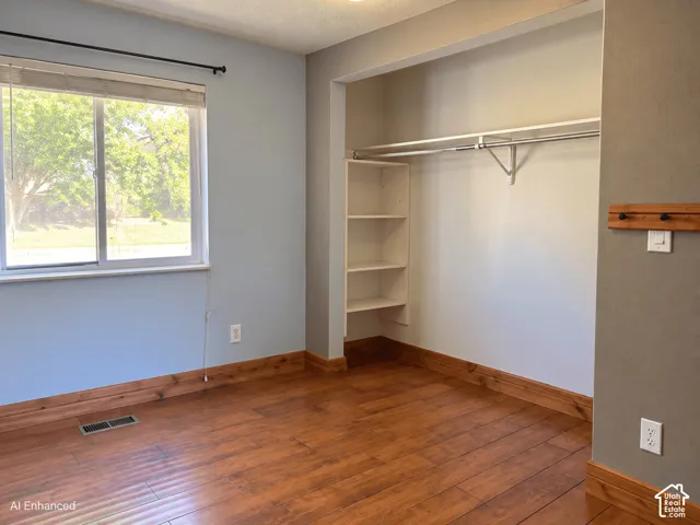 Room featuring wood-finish flooring, natural wood trim, sliding window, and an open closet with integrated shelving and a metal hanging rod