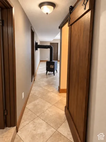 Interior hallway featuring tiled flooring, a wooden sliding barn door, and a freestanding wood-burning stove with a metal flue