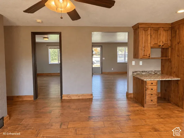 Wood-finish flooring, built-in wooden cabinetry, multi-drawer desk workstation, stone-composite countertop, and ceiling-mounted light fixture with fan