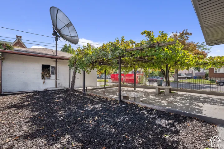 Outdoor space featuring a paved patio area, an overhead metal-frame trellis, stone-style benches, and dark organic mulch ground cover