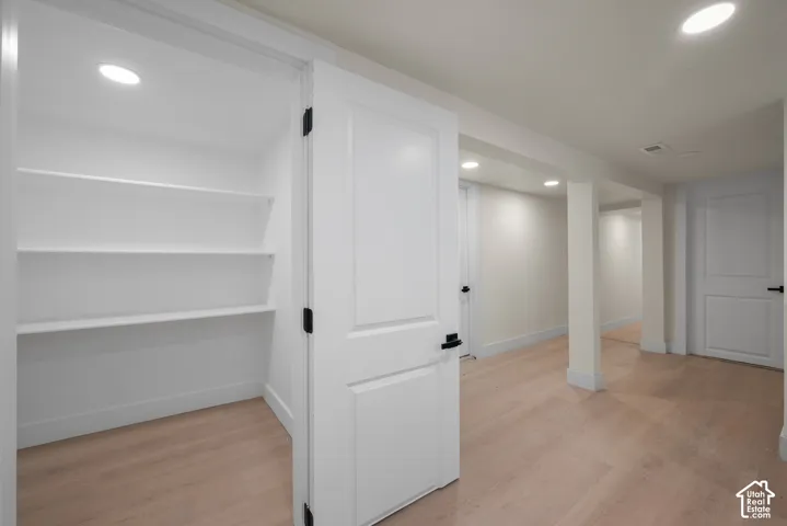 Storage closet featuring built-in shelving, wood-finish flooring, recessed lighting, white panel doors, and matte black hardware