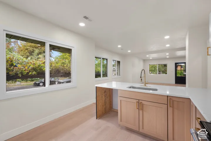 Kitchen featuring light-tone wood cabinetry, white stone countertops, an undermount sink with a gold-tone gooseneck faucet, light-tone wood-finish flooring, and recessed ceiling lighting