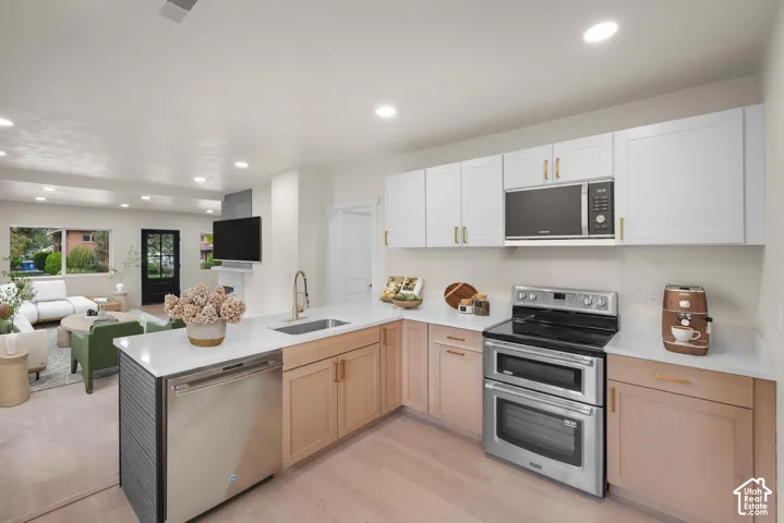 Kitchen featuring two-tone cabinetry, quartz countertops, a stainless steel double-oven range, an undermount sink with a gooseneck faucet, and wood-finish flooring