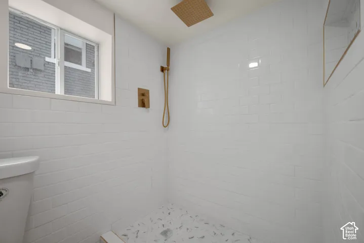 Walk-in shower featuring white subway tile surround, metallic brass-finish rainfall showerhead with handheld attachment, built-in tiled niche, and stone-patterned floor tile