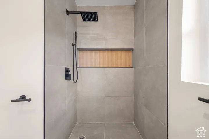 Walk-in shower featuring large-format grey tile, a built-in recessed niche with wood-finish backing, a rainfall showerhead, and matte black fixtures
