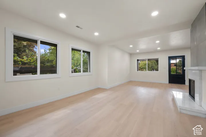 Interior space featuring light wood-finish flooring, recessed lighting, expansive windows, a stone-surround fireplace with a hearth, and a glass-paneled exterior door