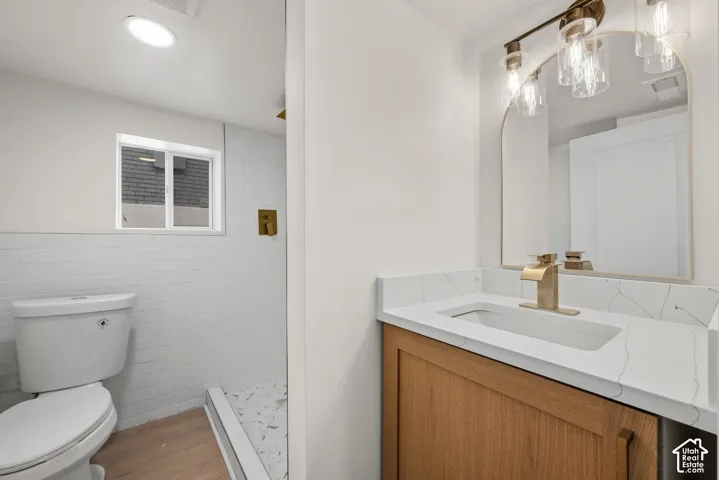 Bathroom vanity featuring wood-finish cabinetry, a stone-composite countertop with integrated sink, brass-tone hardware, and an arched mirror with three-light fixture