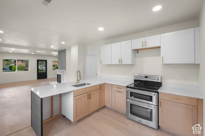 Kitchen featuring two-tone cabinetry with gold-tone hardware, white stone countertops, stainless steel dual-oven range, recessed lighting, and wood-finish flooring