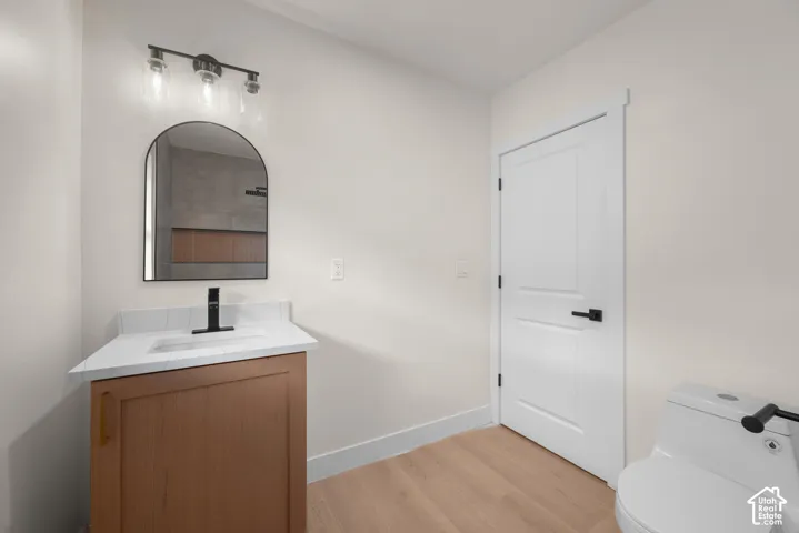 Bathroom featuring a wood-finish vanity, white countertop with integrated sink, matte black plumbing fixtures, arched mirror, and wood-finish flooring
