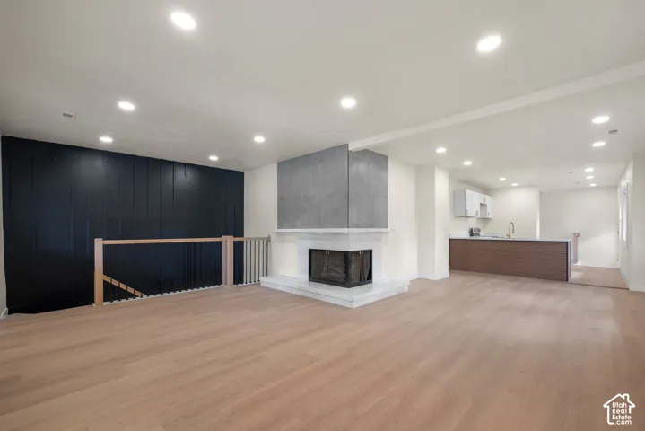 Open-concept interior featuring light wood-finish flooring, recessed lighting, a corner fireplace with stone surround and hearth, black vertical-panel accent wall, and wood-railing staircase