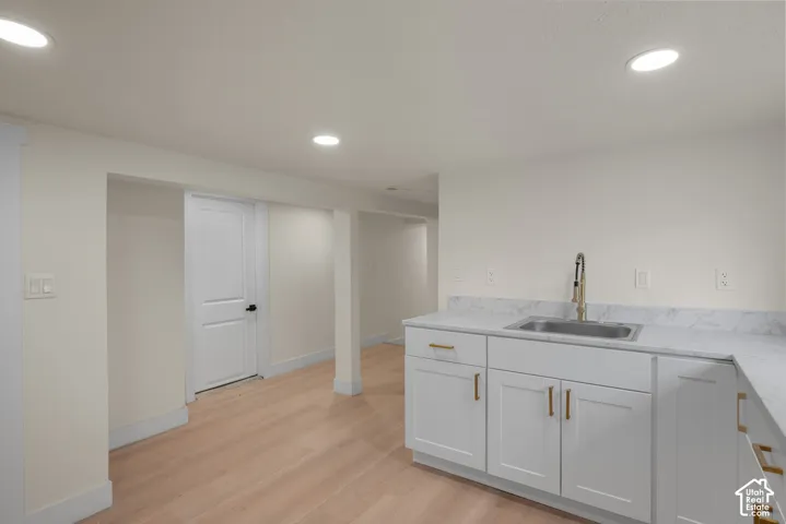 Kitchenette featuring white Shaker-style cabinetry, stone-finish countertops, stainless steel undermount sink with high-arc faucet, recessed lighting, and wood-finish flooring