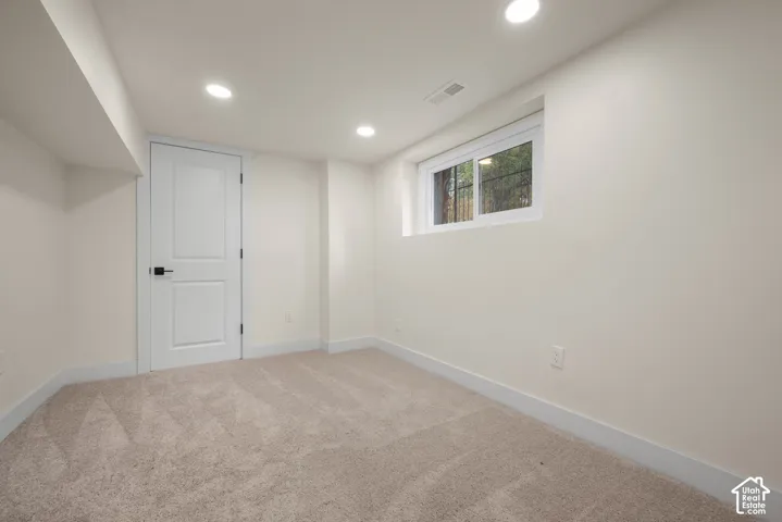 Neutral interior room featuring neutral carpeting, recessed lighting, a single-panel interior door with matte black hardware, and a sliding window