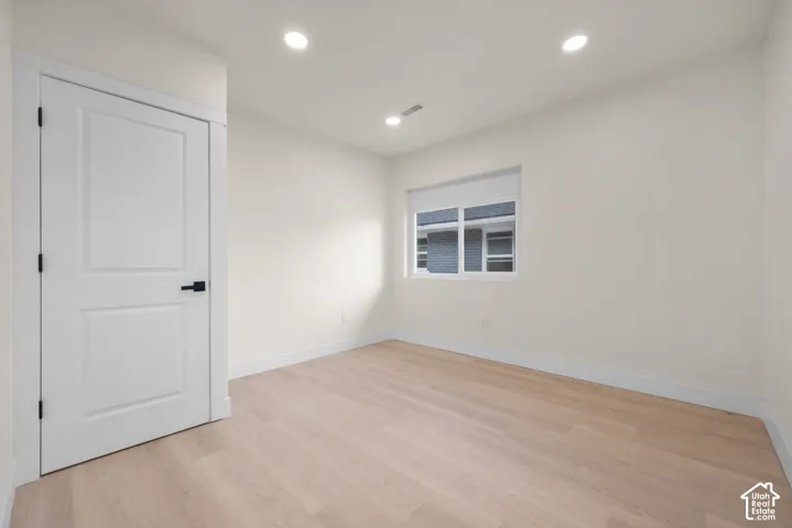 Neutral-toned room featuring wood-finish flooring, recessed lighting, a sliding window with a roller shade, and a paneled interior door with matte black hardware