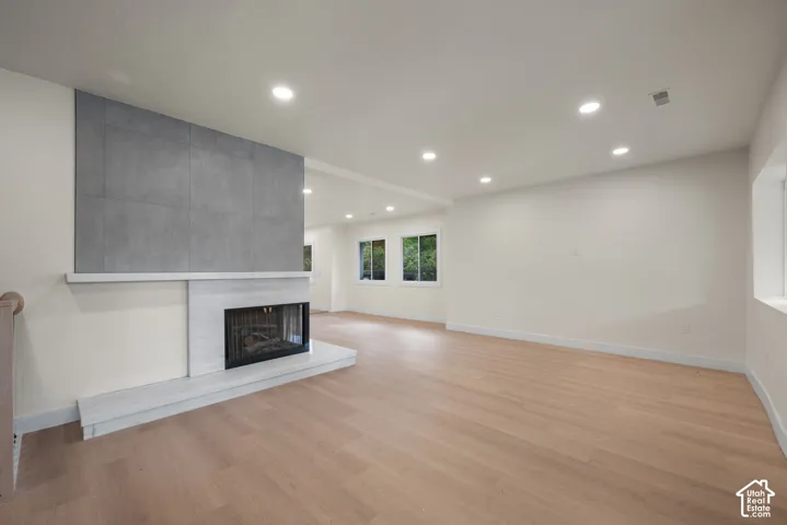 Living area featuring wood-finish flooring, recessed lighting, and a floor-to-ceiling fireplace with a stacked-stone finish and a stone-surface hearth