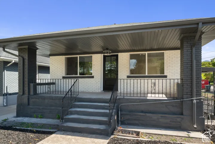 Covered front porch featuring a painted brick exterior, concrete steps, wrought iron railing, and a modern glass-panel entry door