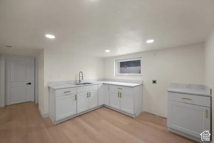 White shaker-style cabinetry featuring brass-tone hardware, stone-finish countertops, stainless steel sink with high-arc pull-down faucet, recessed lighting, and wood-finish flooring