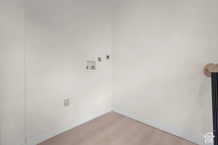 Laundry area featuring wood-finish flooring, recessed water supply valves, and an integrated dryer vent