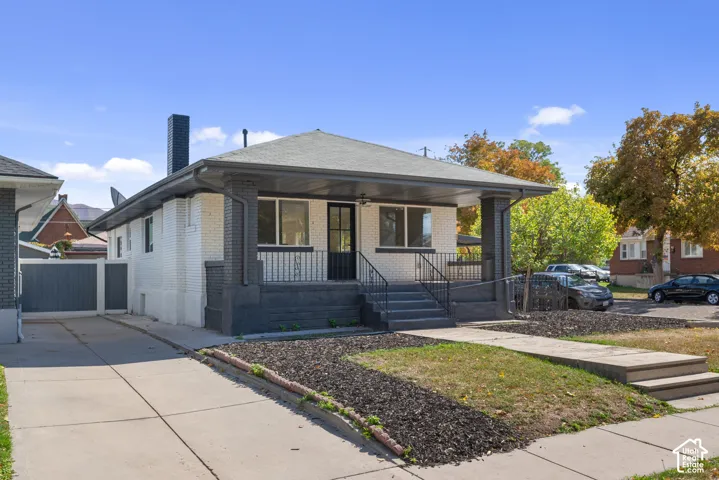 Single-story residence featuring white brick siding, a covered front porch with concrete steps, wrought iron railings, and a side concrete driveway