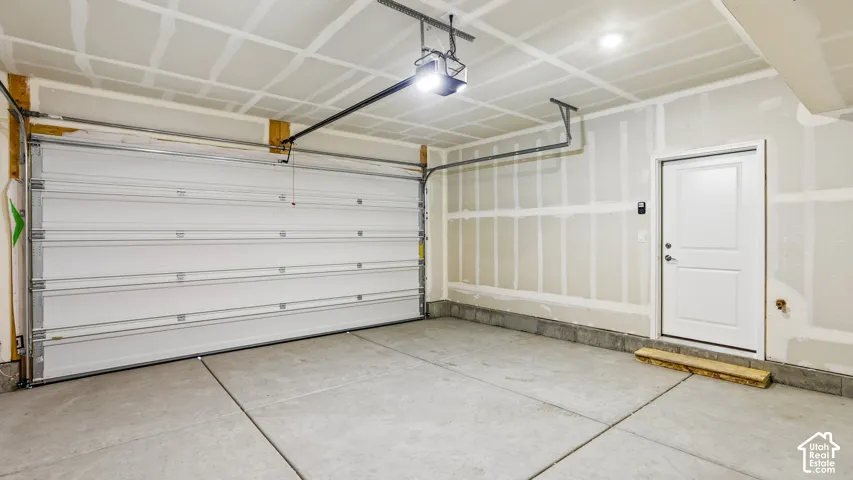 Attached two-car garage featuring a sectional overhead door, automated door opener, concrete flooring, and an exterior-grade pedestrian door
