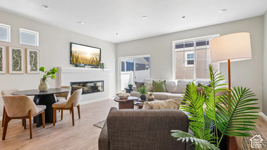 Open-concept living space featuring wood-finish flooring, recessed lighting, horizontal linear fireplace with a mantle, and glass sliding door access to exterior space