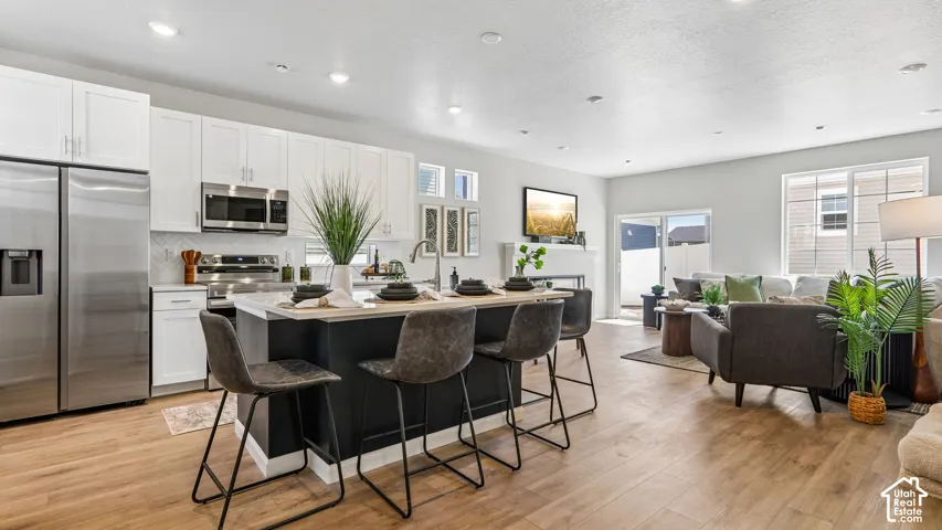 Kitchen featuring white shaker-style cabinetry, quartz countertops, a central island with a contrasting dark base, stainless steel appliances, and wood-finish flooring