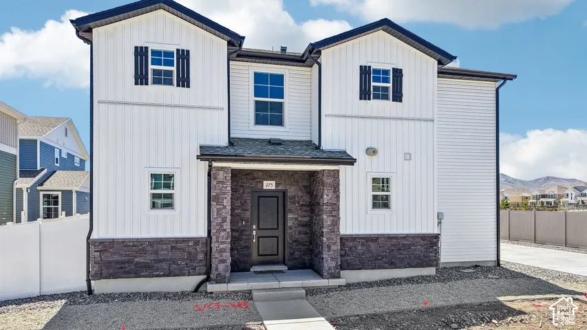 Two-story residence featuring a board-and-batten facade, stone veneer accents, multi-pane windows with shutters, and a covered entryway
