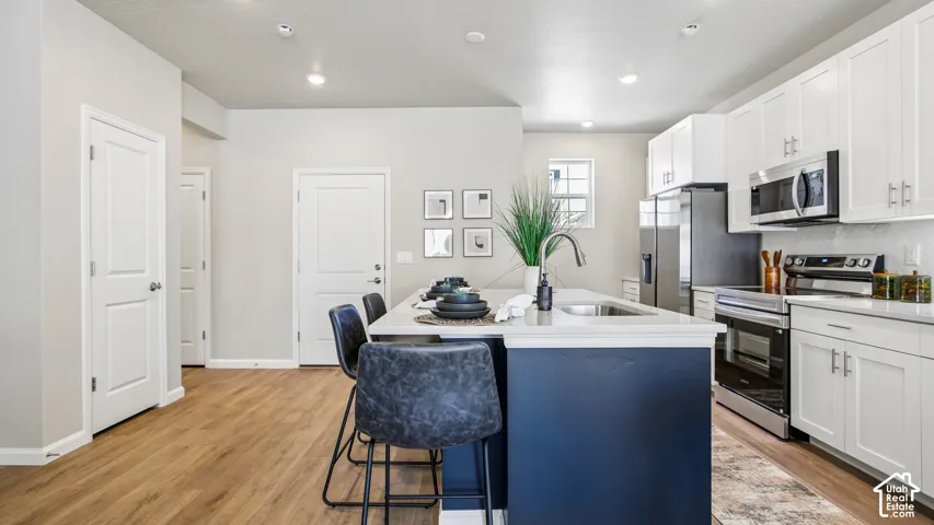 Kitchen featuring an island with a stone-finish countertop and undermount sink, white cabinetry, stainless steel appliances, and wood-finish flooring