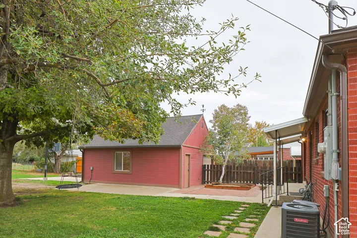 Backyard featuring a red brick exterior, detached structure with gable roof, concrete patio, and stone paver walkway