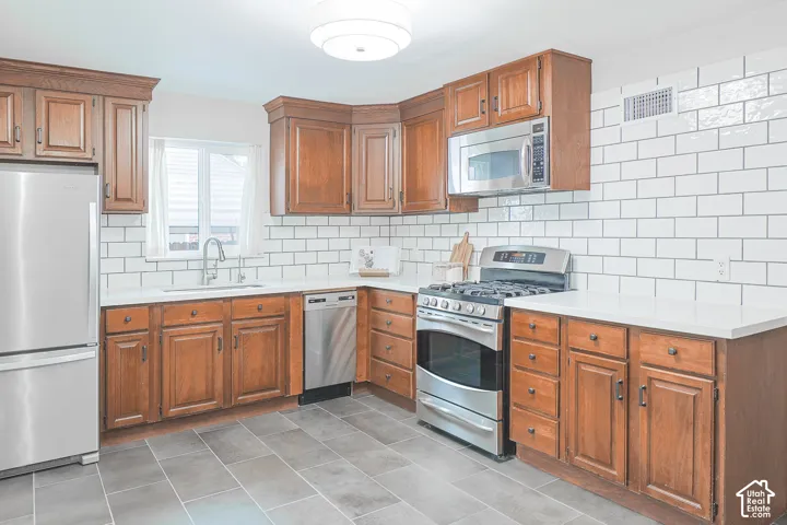 Kitchen featuring stained wood cabinetry, white subway tile backsplash, solid-surface countertops, stainless steel appliances, and large-format tile flooring
