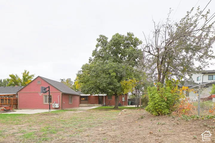 Backyard space featuring a detached garage with siding, concrete patio, mature trees, and chain-link perimeter fencing