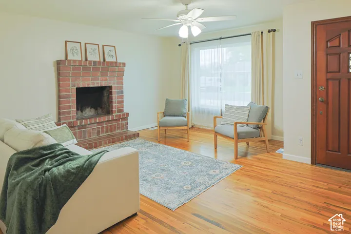 Living area featuring wood-finish flooring, a full-height brick fireplace, a ceiling fan with integrated lighting, and a solid wood front door with decorative paneling