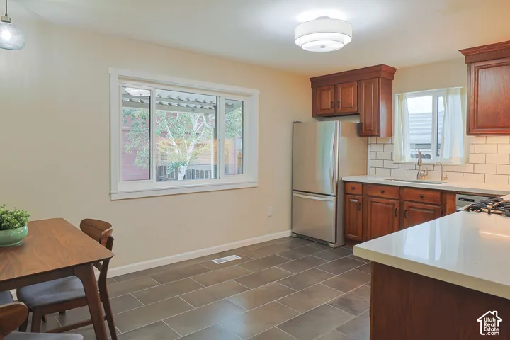 Kitchen featuring wood cabinetry, stainless steel refrigerator, white tile backsplash, light-toned countertops, and large-format tile flooring