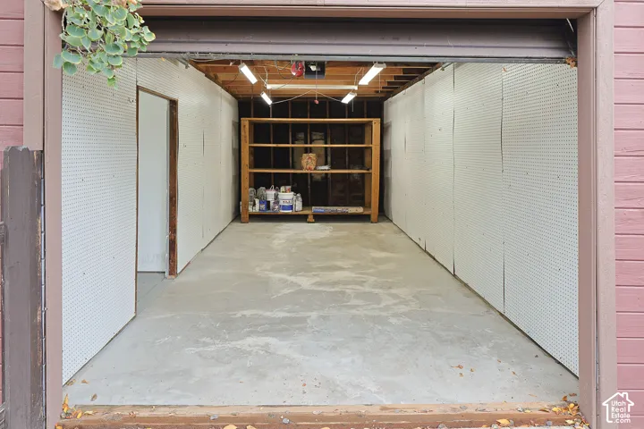 Garage featuring concrete flooring, pegboard wall panels, built-in wooden shelving, and linear overhead lighting